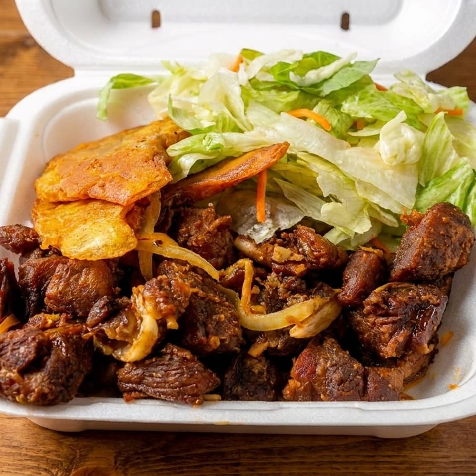Fried pork chunks with plantain chips and a side salad in a white takeout container.